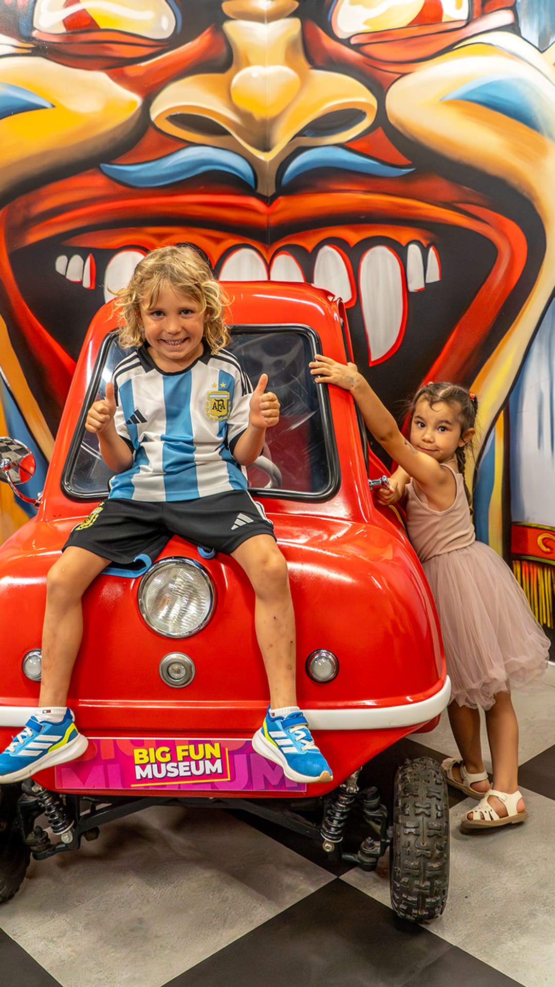 Two children posing with the world's smallest car in front of a colourful monster mural at Guinness Records Museum Barcelona